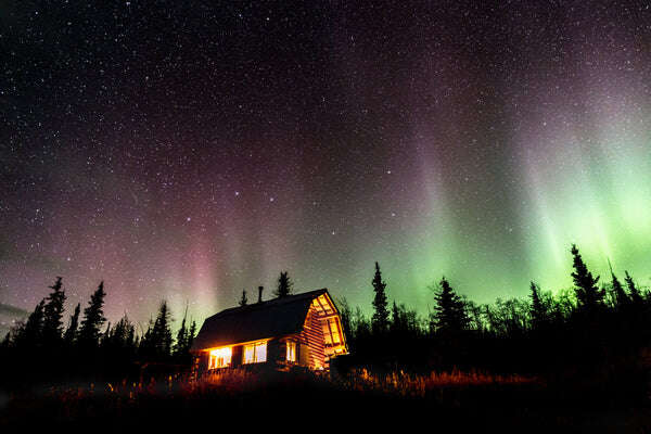Cabin with lights in the dark woods with aurora borealis in background